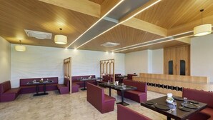 A restaurant with wooden ceiling beams, marble flooring, and red upholstered booths and tables. - Vinti Resort, Ambaji (Danta)