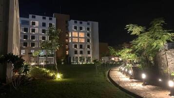A nighttime view of a hotel with illuminated windows and a well-lit garden area.