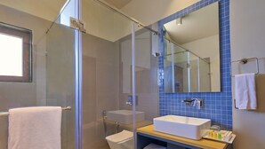 A bathroom with a glass-enclosed shower, a white sink, and a blue-tiled wall. - Vinti Resort, Ambaji (Danta)