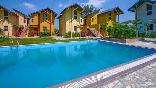 A swimming pool with a stone border, surrounded by yellow buildings with steps leading to the entrance. - Vinti Resort, Ambaji (Danta)