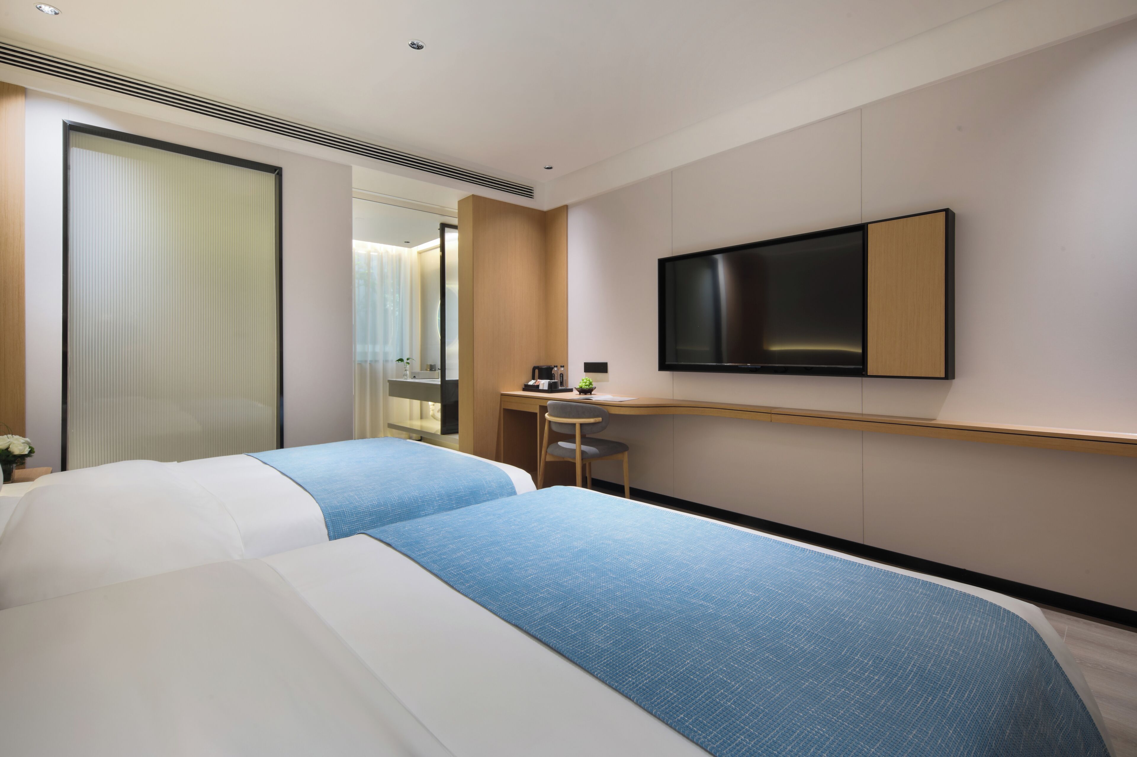 Habitación de hotel con dos camas, un escritorio, una silla, un televisor y una ventana con cortinas.