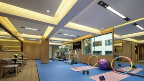 A modern gym with exercise equipment, mats, and a seating area with tables and chairs.