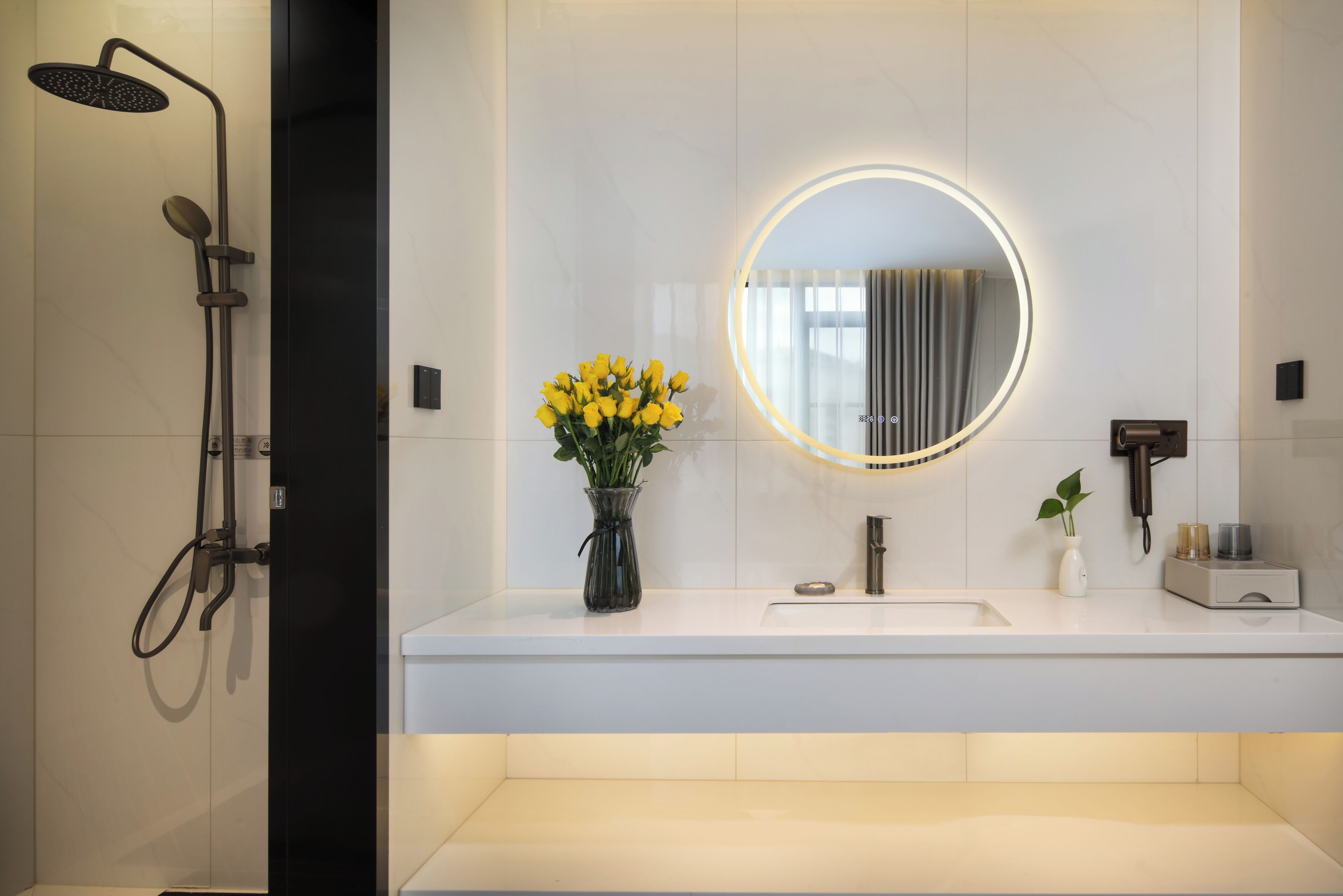 Une salle de bain moderne avec une douche, un lavabo, un miroir et un vase rempli de fleurs jaunes.