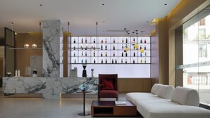 A modern hotel lobby with a marble reception desk, a red armchair, a sofa, and a wall of liquor bottles.