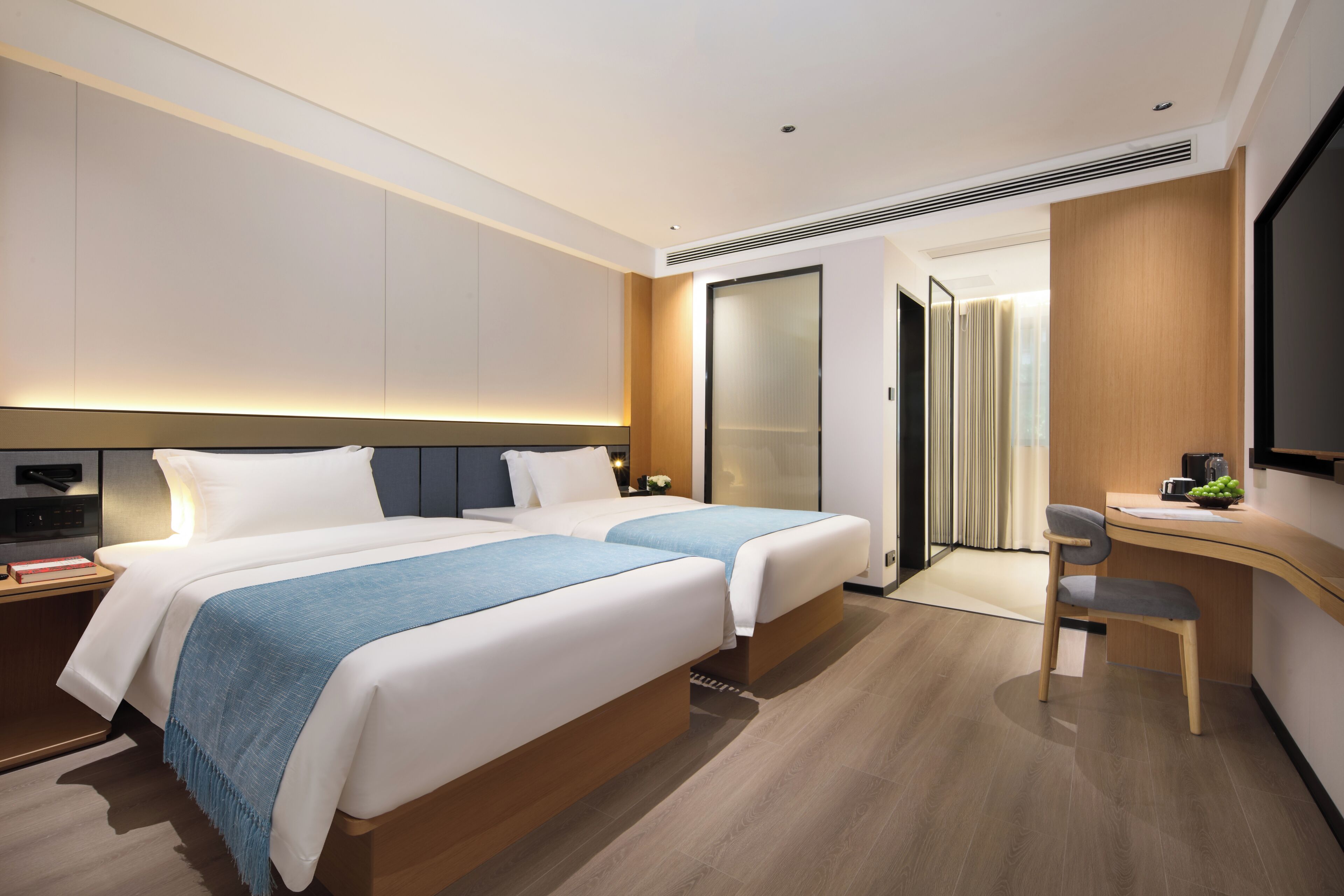 A hotel room with two beds, a desk, a chair, and a TV.