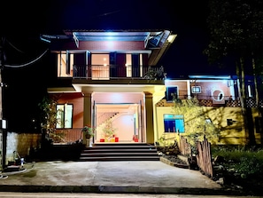 A two-story house with a balcony, a staircase leading to the entrance, and a well-lit front yard.