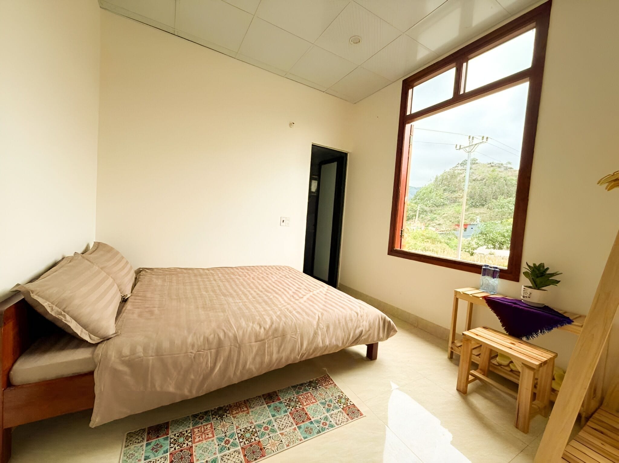 A bedroom with a bed, a small table, a window with a view, and a door.