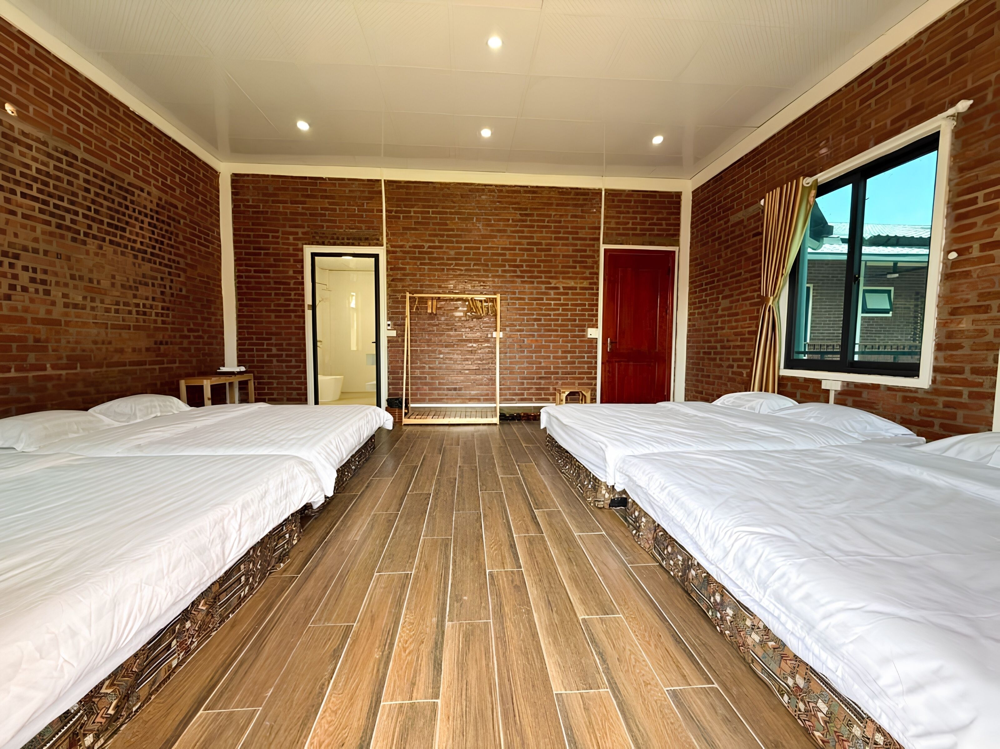 Een hotelkamer met twee bedden, een bakstenen muur, een houten vloer, een raam en een deur.