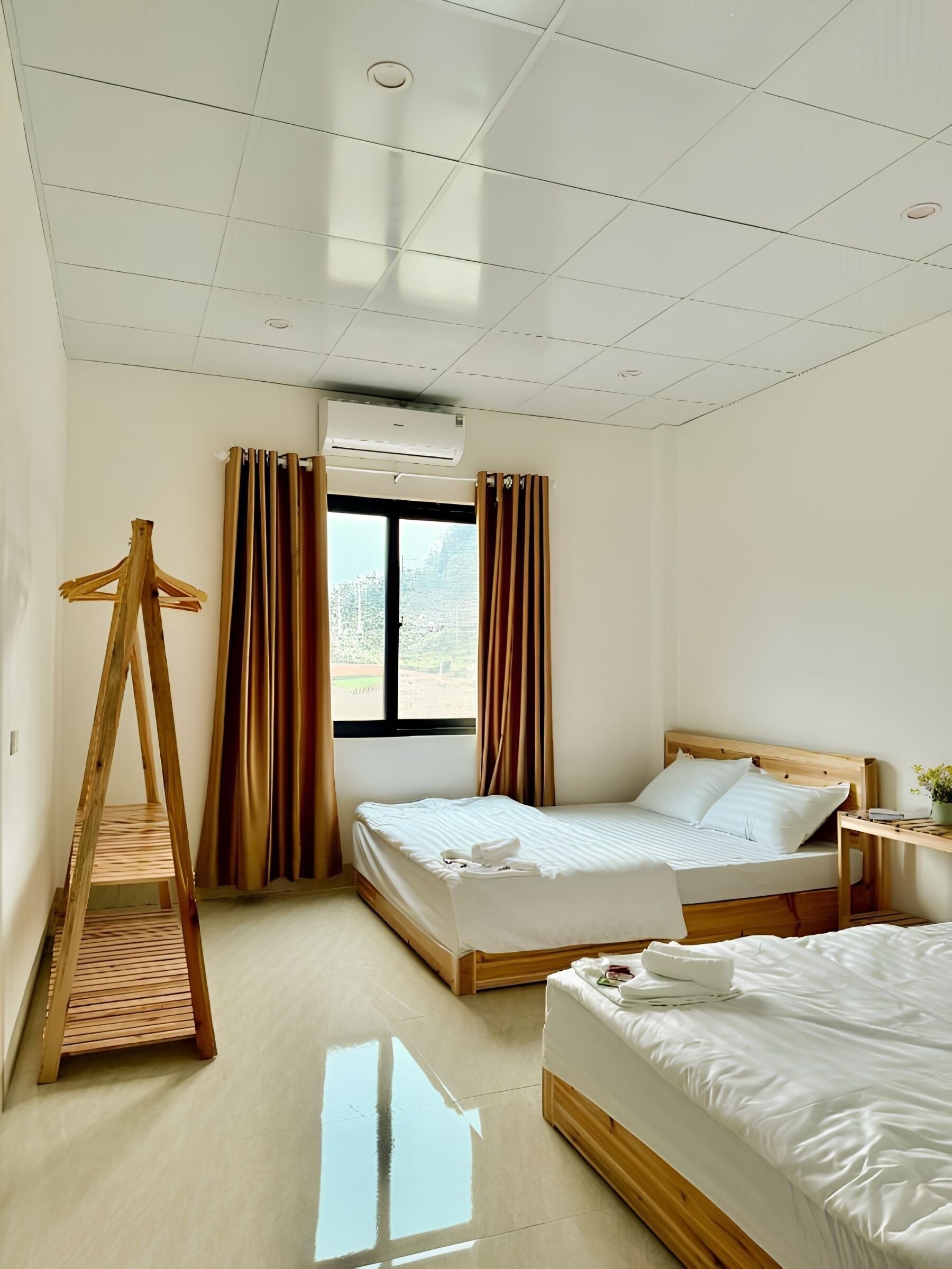 A hotel room with two beds, a wooden ladder, a window with curtains, and an air conditioning unit.