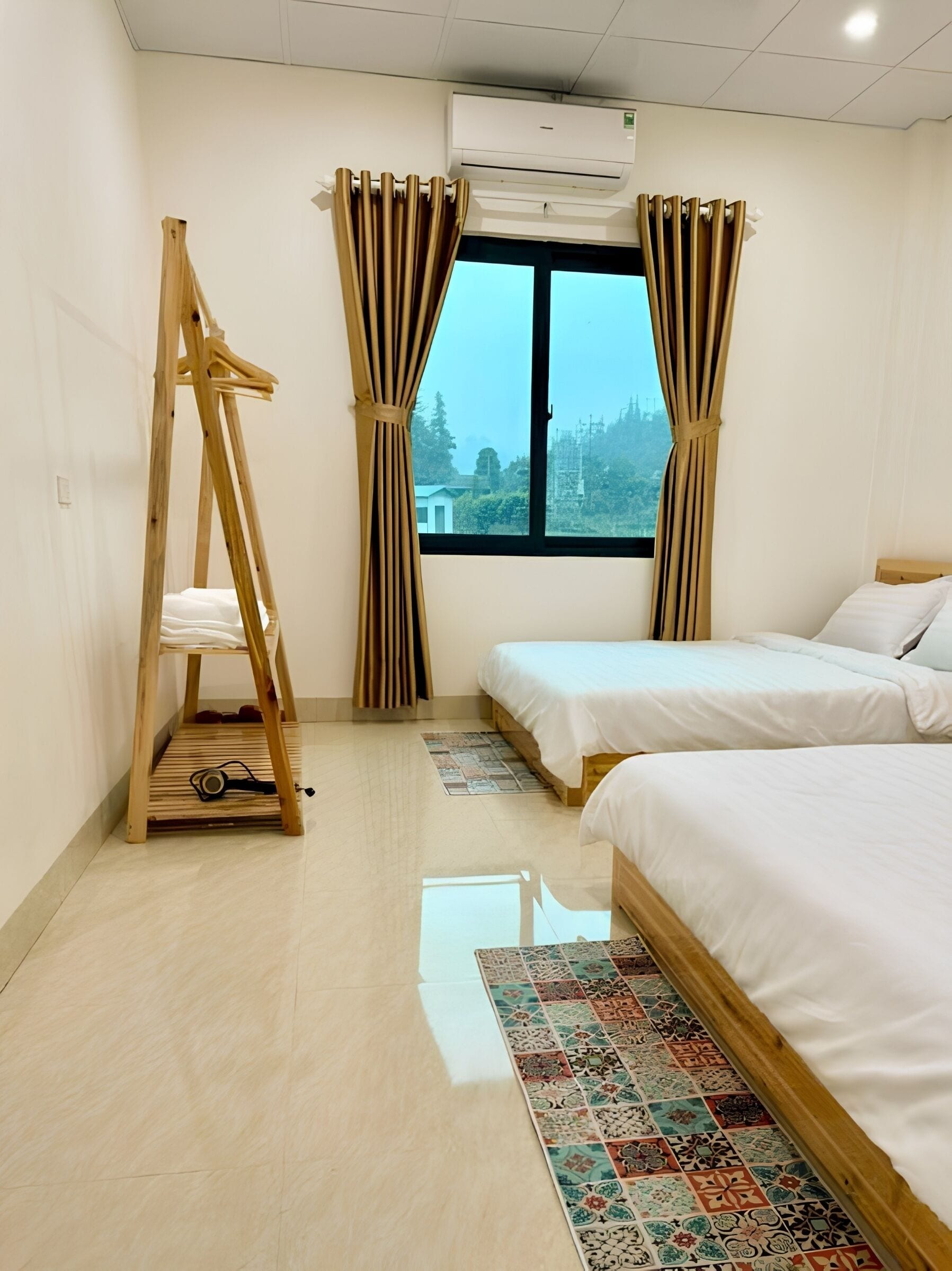 A bedroom with two beds, a wooden ladder, a window with curtains, and an air conditioning unit.