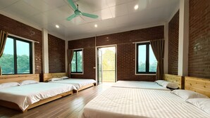 Habitación de hotel con tres camas, suelo de madera, paredes de ladrillo y ventanas grandes.