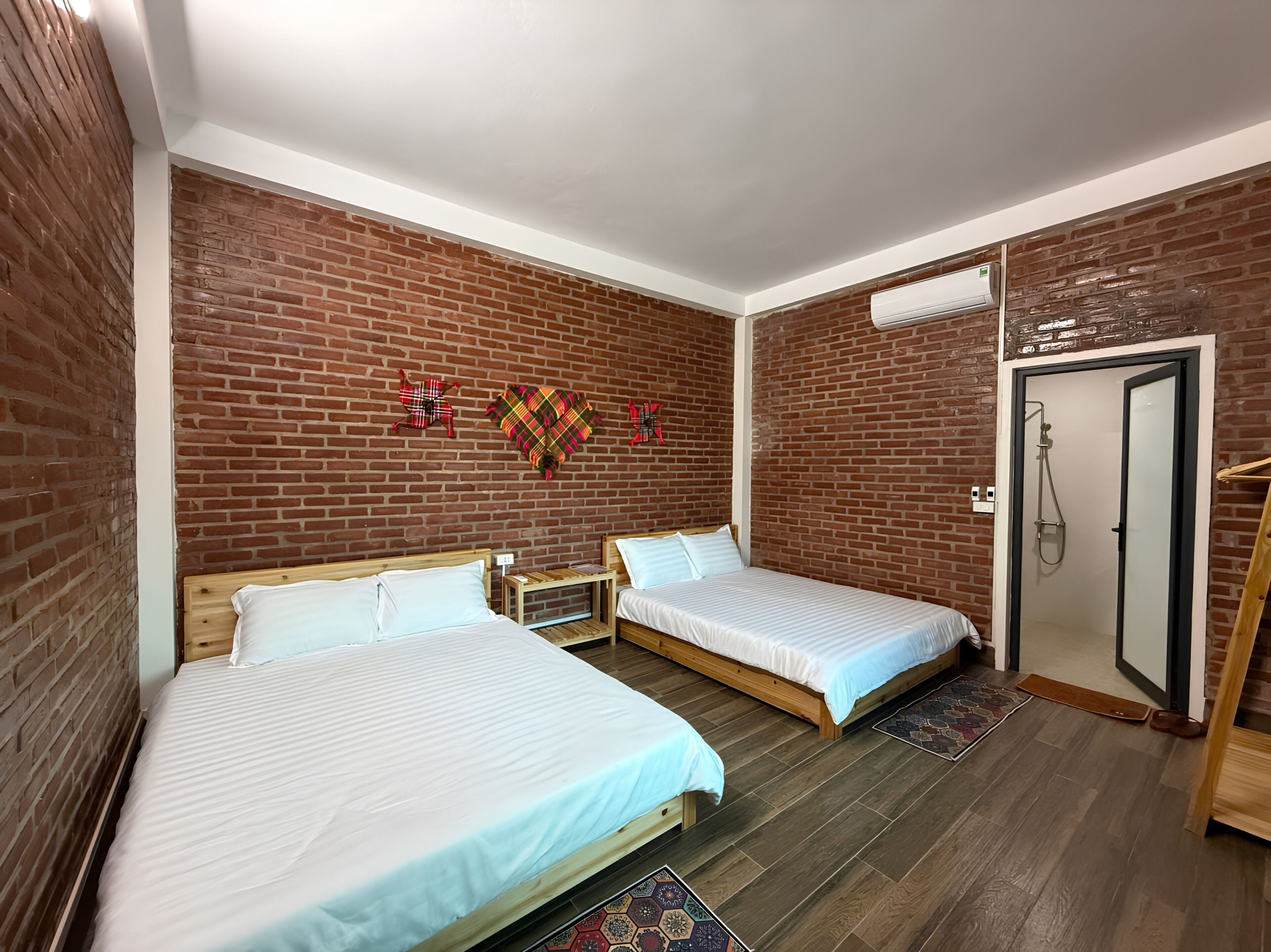 A hotel room with two beds, a brick wall, a wooden floor, and a shower area.