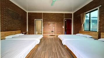 Une chambre d’hôtel avec deux lits, un plancher en bois, des murs en briques, un ventilateur au plafond et une fenêtre avec des rideaux.