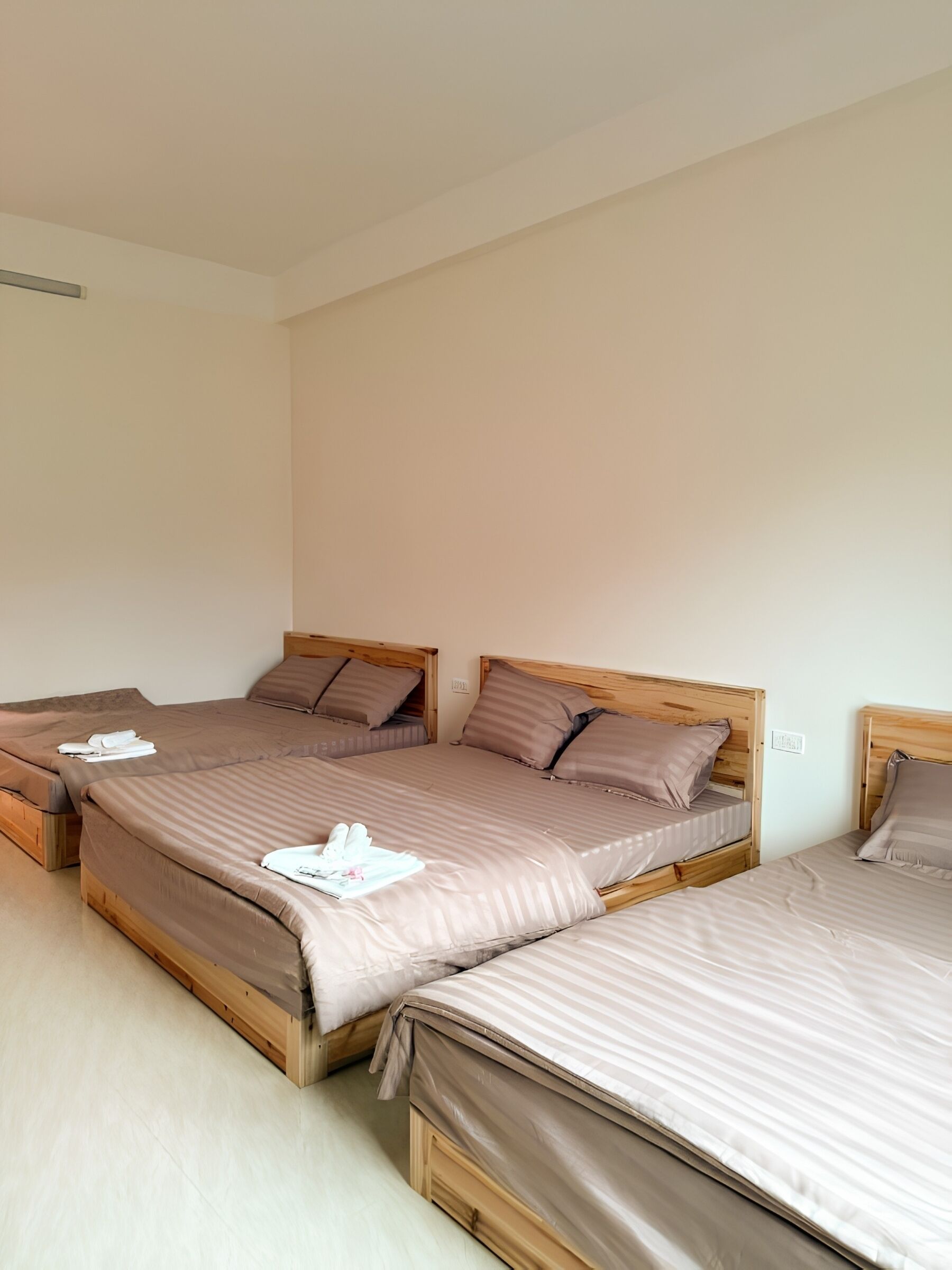 Habitación de hotel con tres camas de madera, cada una con cabecero y almohadas.