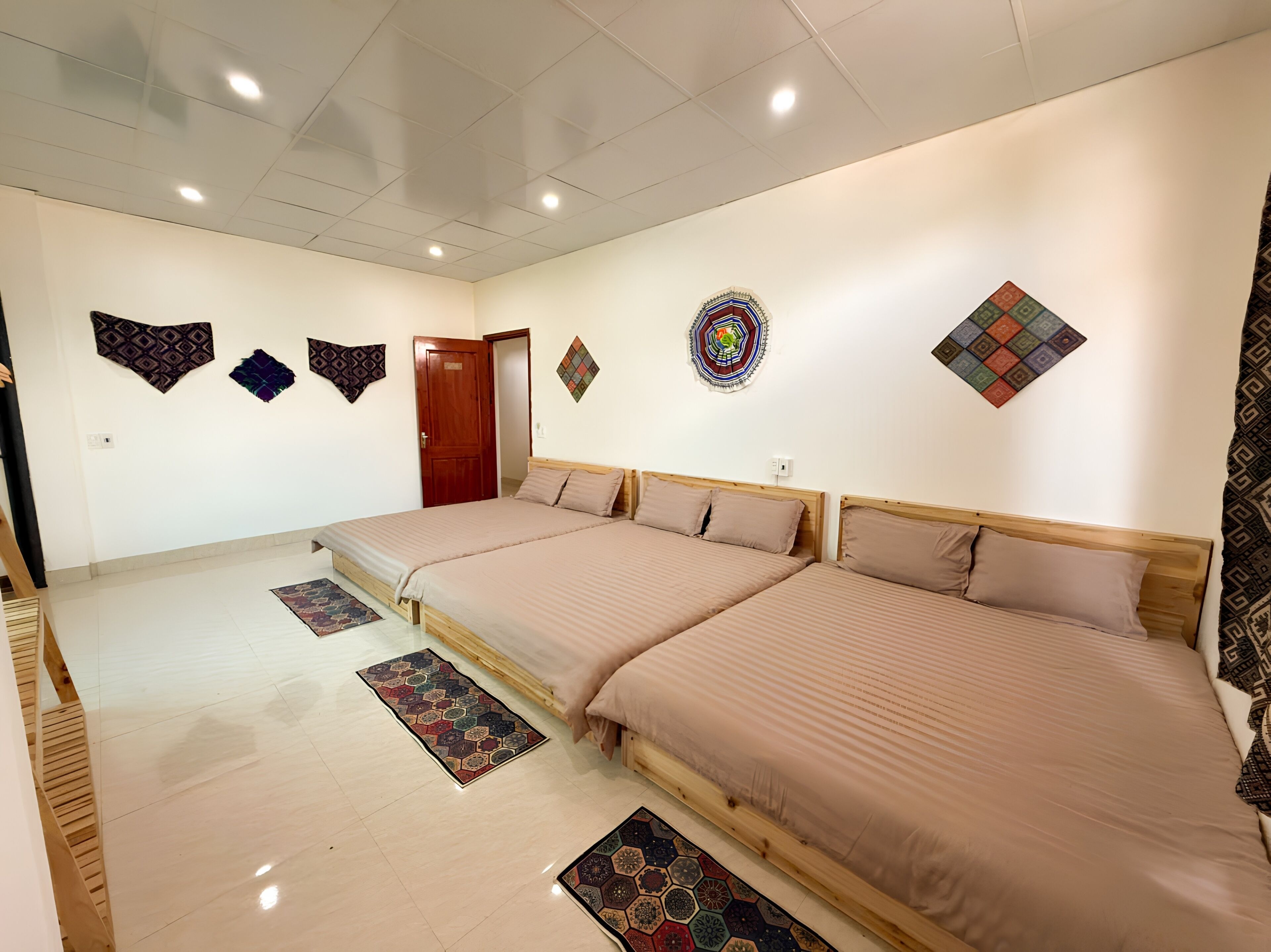 A room with two beds, a wooden door, and patterned rugs on the floor.
