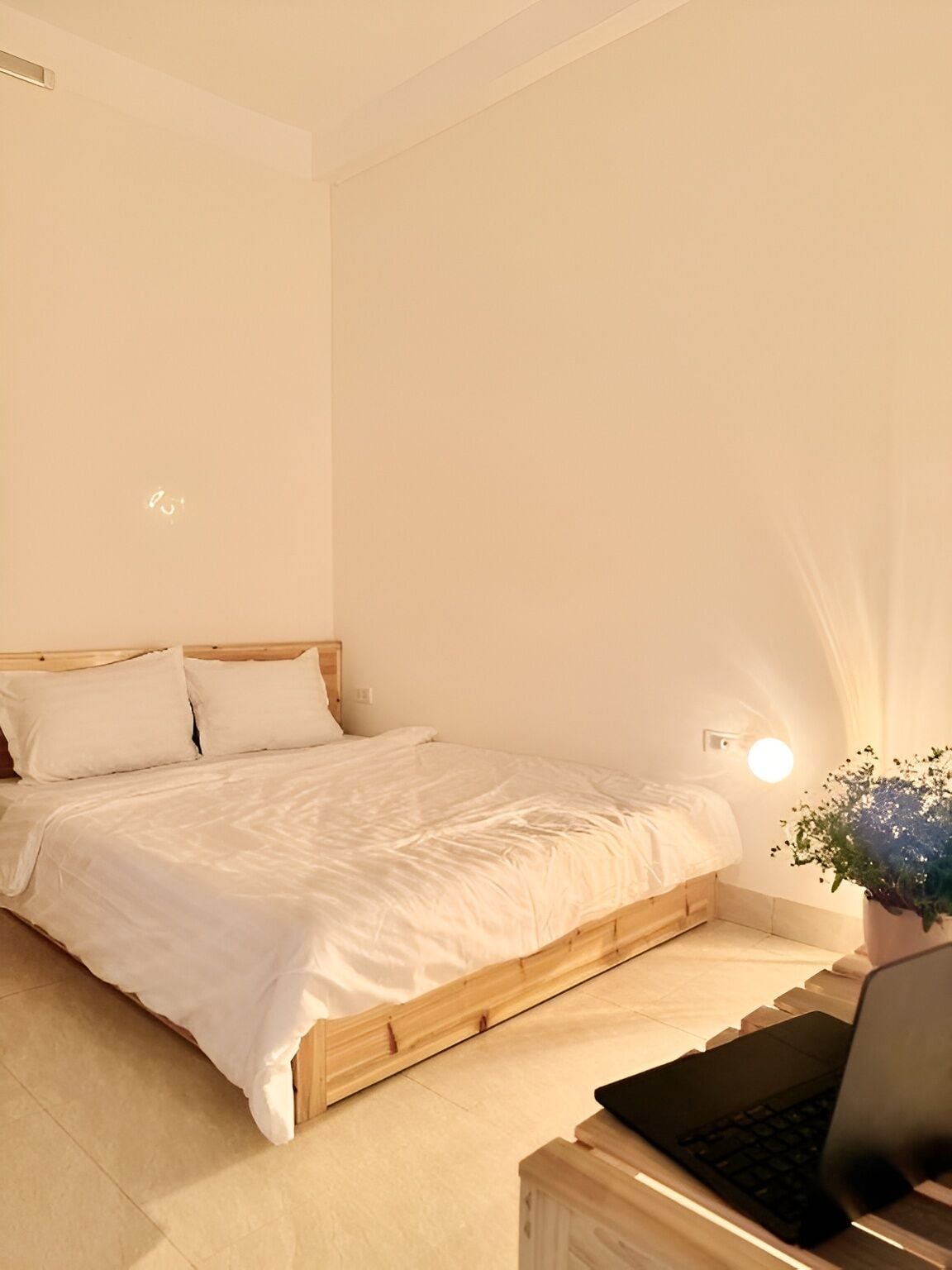 Une chambre à coucher avec un lit en bois, une table de chevet sur laquelle se trouve un ordinateur portable et une lampe fixée au mur.
