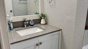 Une salle de bain avec un lavabo blanc, un miroir, un porte-serviettes et une petite plante en pot.