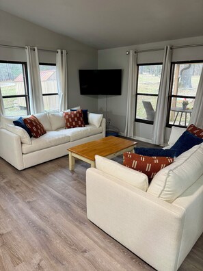 A living room with a white sofa, a wooden coffee table, and a flat-screen TV mounted on the wall. - Beaver Lake Waterfront Retreat (Rogers)