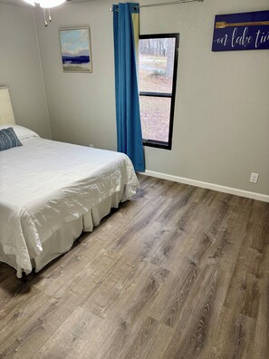 A bedroom with a bed, a window, a painting, and a wall sign. - Beaver Lake Waterfront Retreat (Rogers)