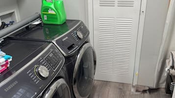 A laundry area with a Samsung washing machine, a green detergent bottle, and a white door with a vent.