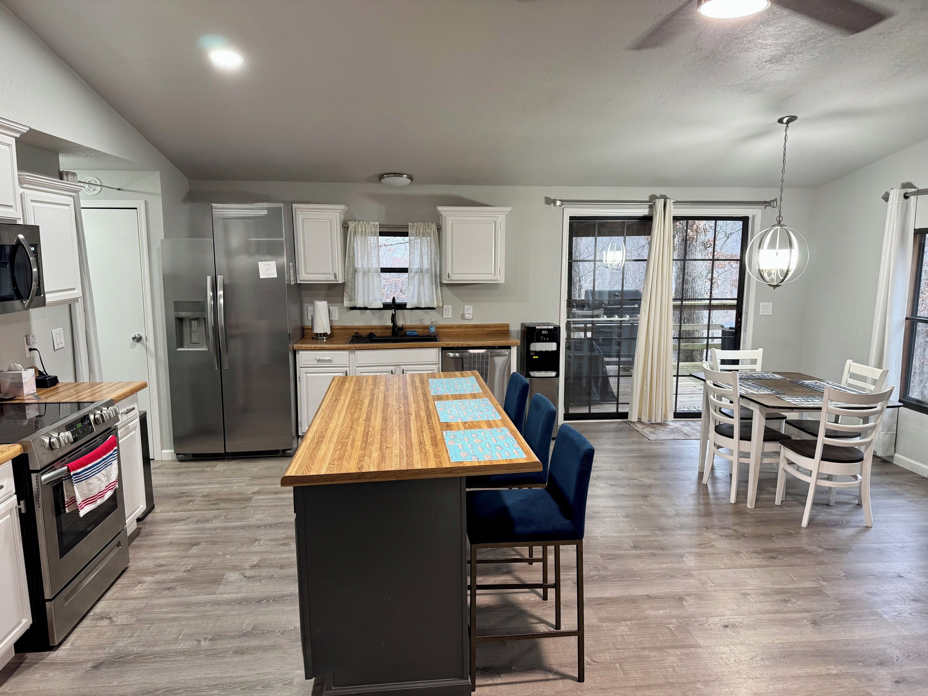 A modern kitchen with a central island, a dining area with a table and chairs, and a view of the outdoors.