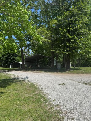 A gravel driveway leading to a covered area with trees and a building in the background. - Beaver Lake Waterfront Retreat (Rogers)