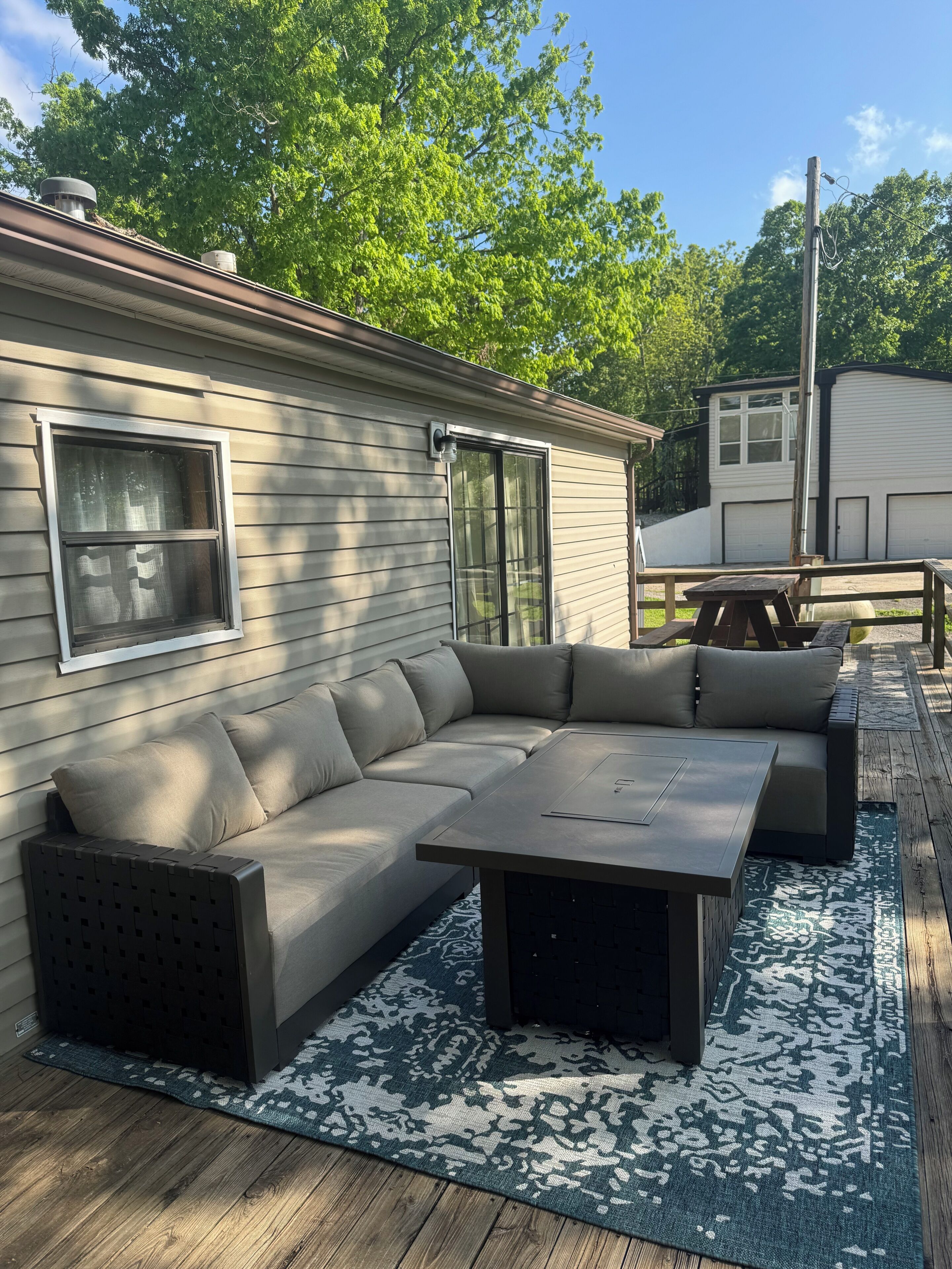 A covered outdoor seating area with a sectional sofa and a table, a patterned rug, and a view of a house with a garage.