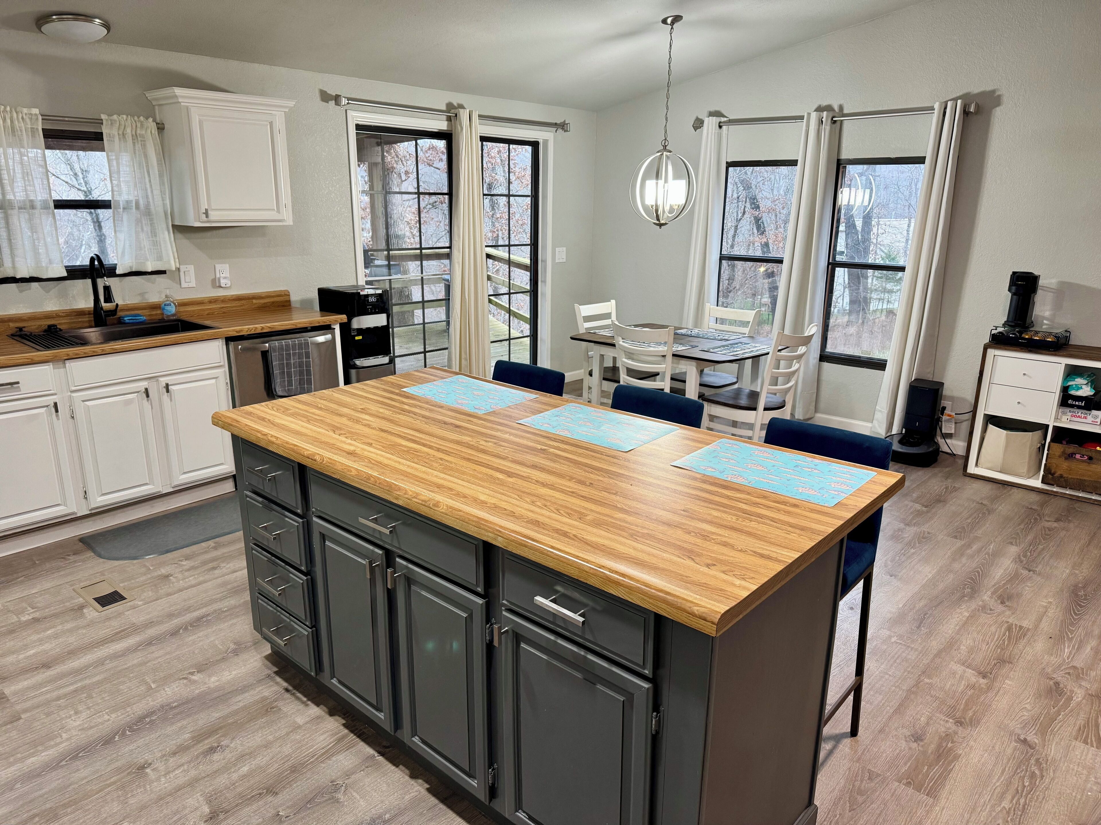 A modern kitchen with a central island, white cabinetry, and a dining area with a table and chairs.