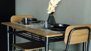 A dining table with four chairs, a vase with flowers, and a black mug. - The One Rooms (Tambon Rawai)