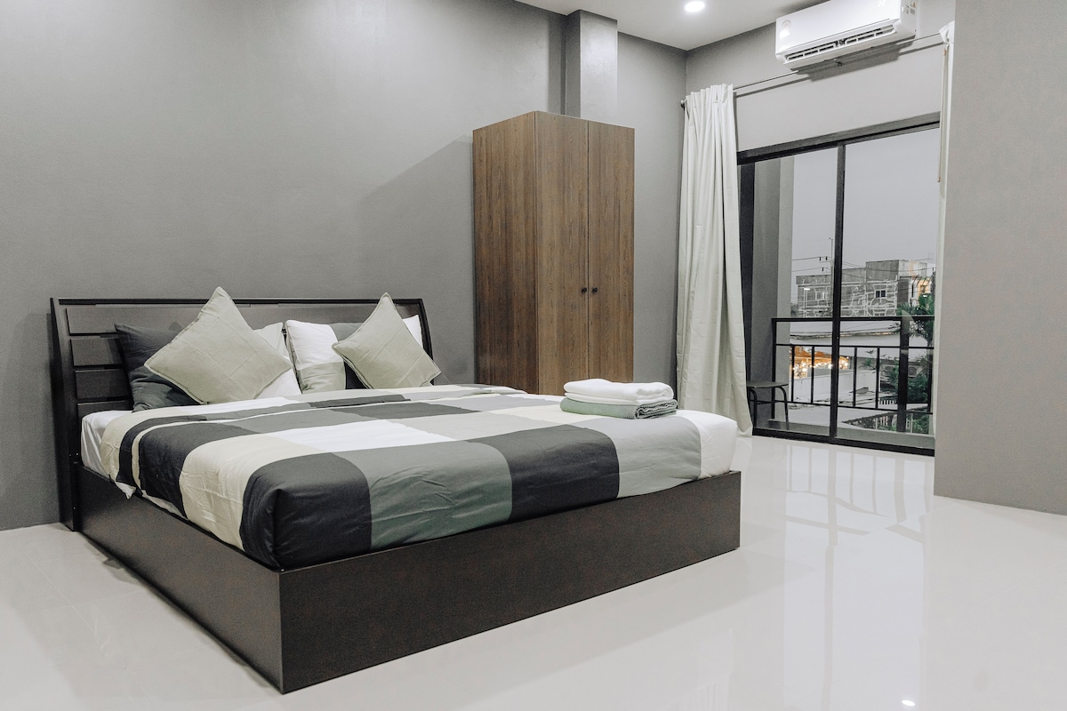 A modern bedroom with a large bed, a wooden wardrobe, and a view of a cityscape through a balcony.