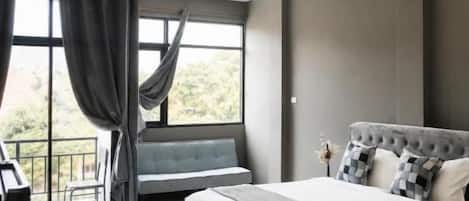 A modern bedroom with a large bed, a bench, and a view of the outdoors.