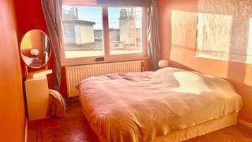A bedroom with a bed, a window, a radiator, and a mirror.