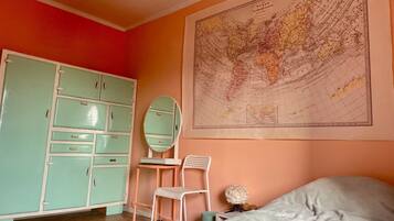 A room with a large world map on the wall, a green wardrobe, a white chair, and a bed with a white pillow.