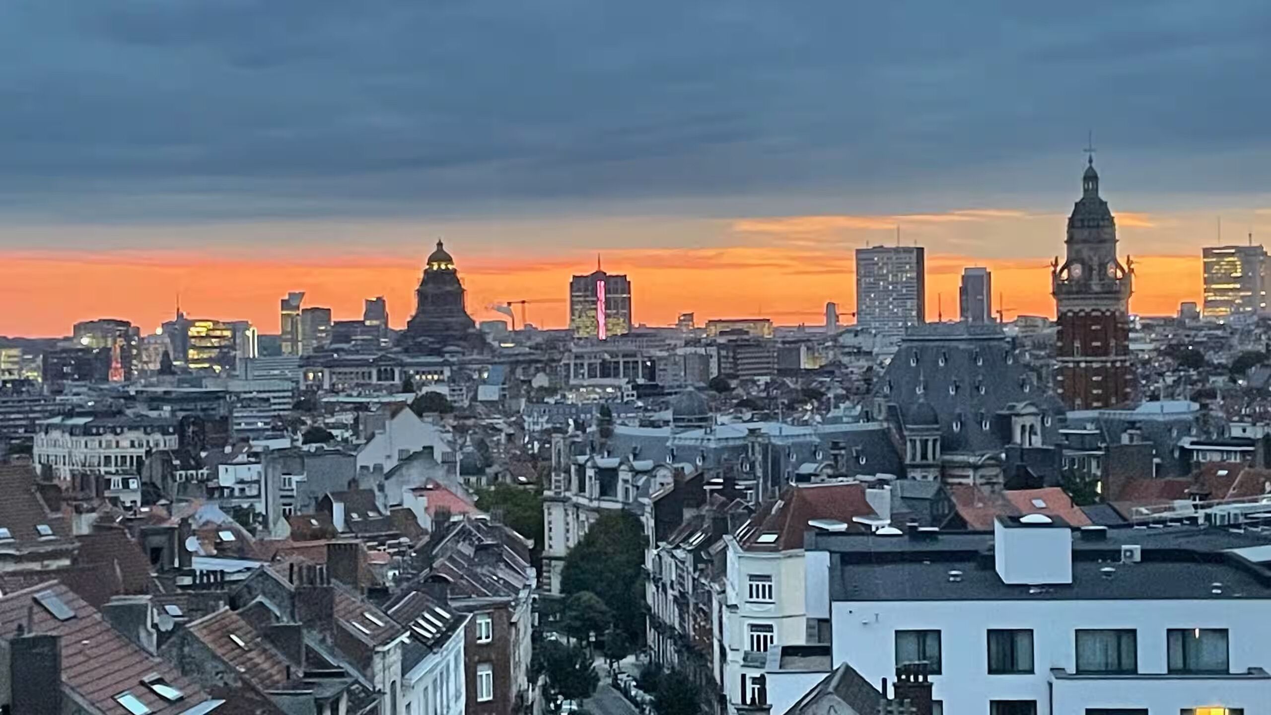 Un paysage urbain avec des bâtiments historiques et des gratte-ciel modernes, sous un ciel au coucher du soleil.