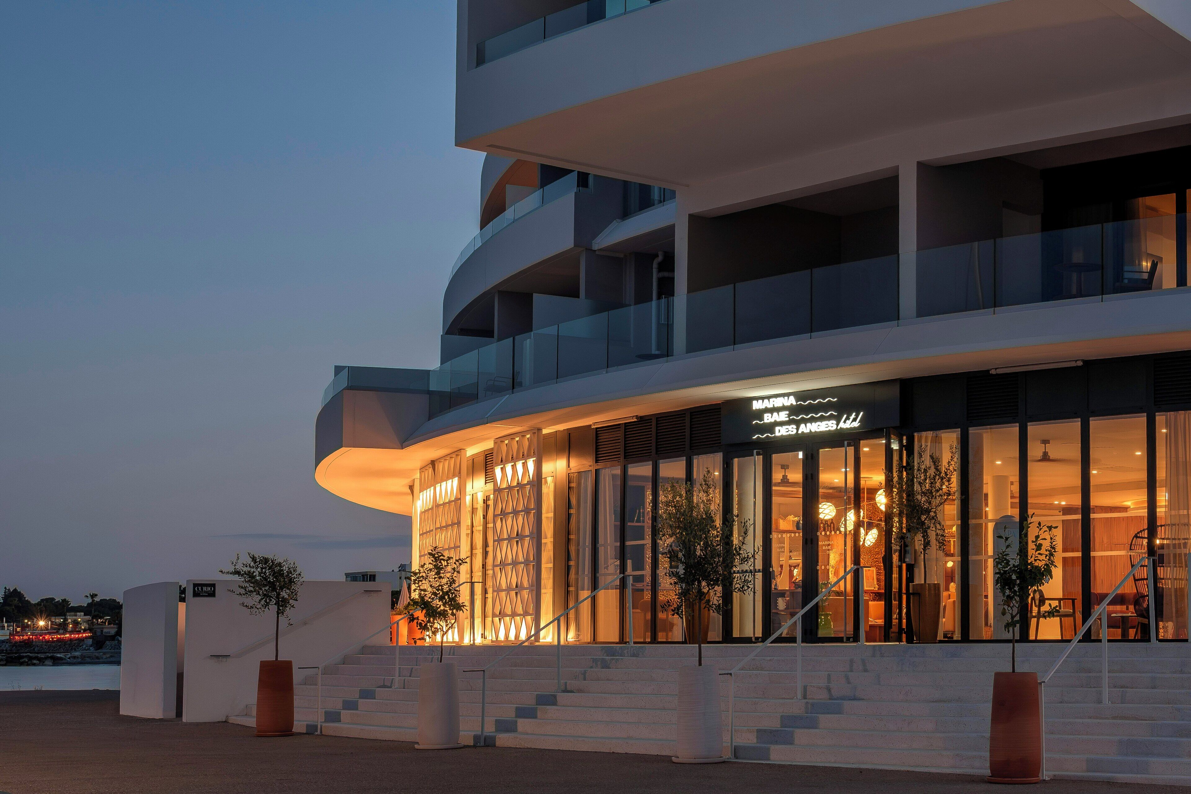 Un hotel moderno con una fachada curva, grandes ventanales y una escalera que lleva a la entrada.