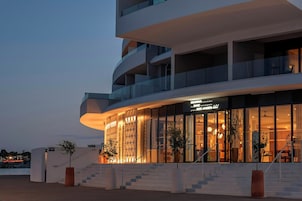 Un hotel moderno con una fachada curva, grandes ventanales y una escalera que lleva a la entrada.
