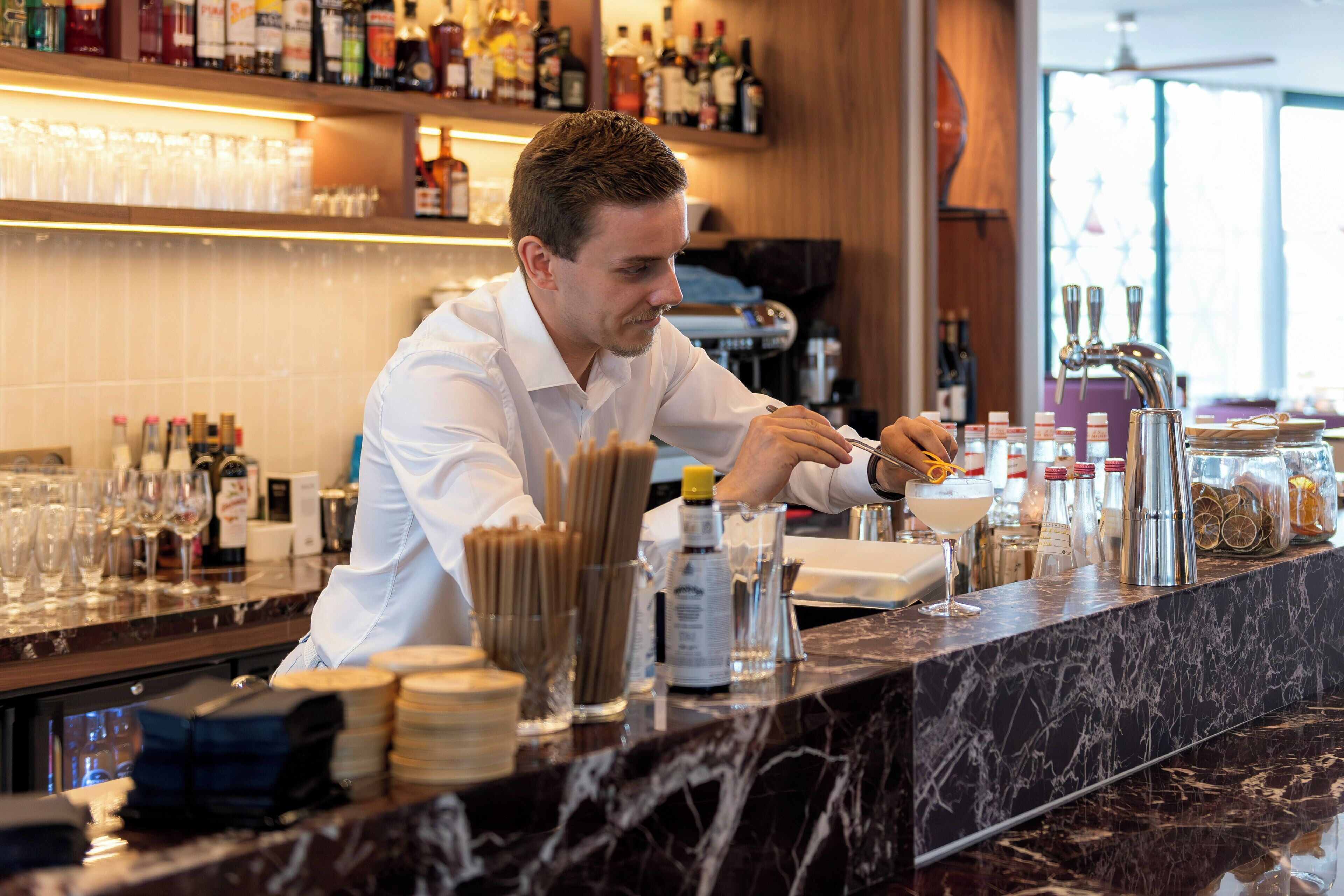 A bartender preparing a drink at a bar with various bottles and glasses.
