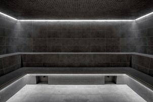 Una piscina interior moderna, con poca luz, paredes de azulejos oscuros y un banco a lo largo del borde.