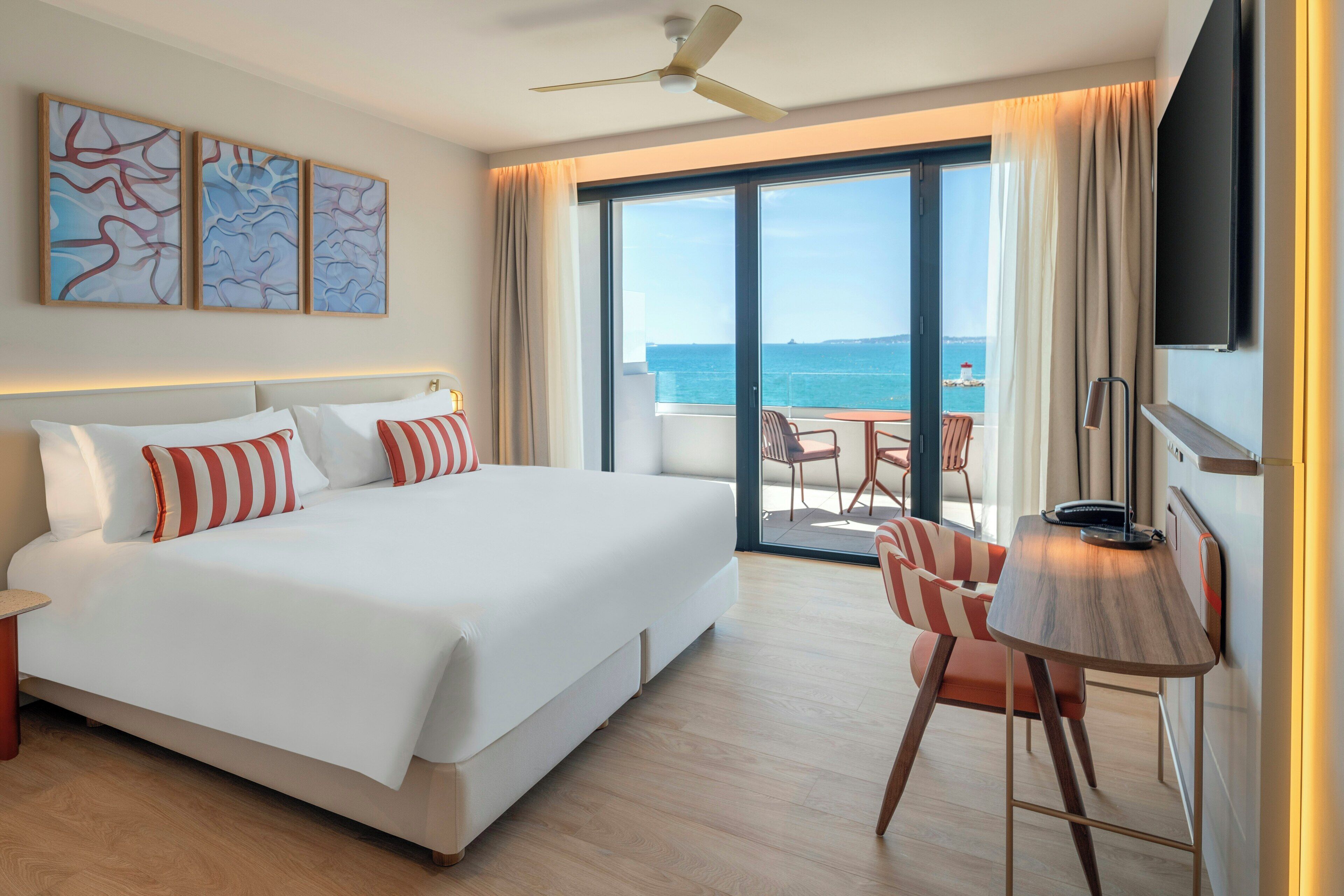 Habitación de hotel con una cama grande, un escritorio con silla, un ventilador de techo y vista al mar.