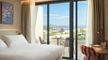 Une chambre d’hôtel avec un lit, une chaise, une table et une vue sur la mer et les bateaux.