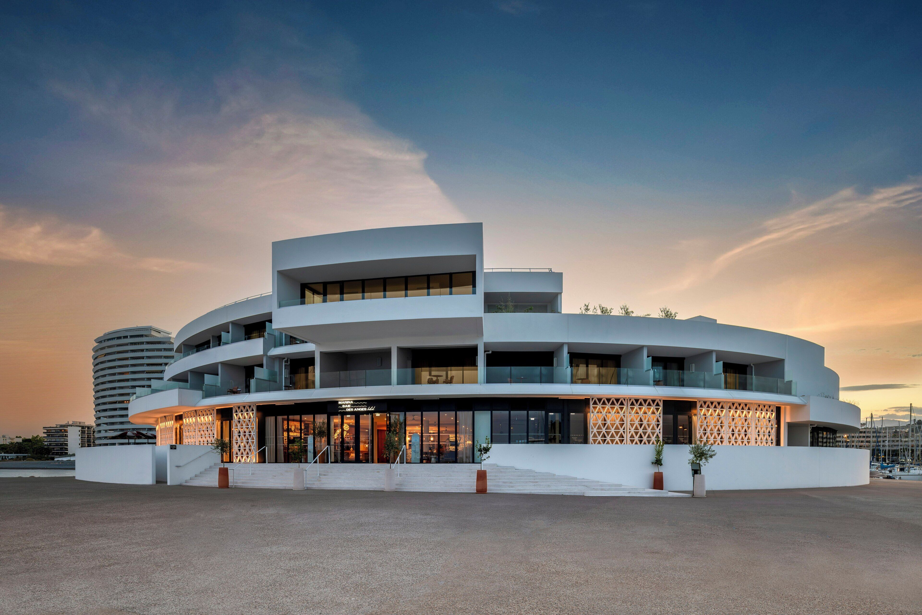 A modern hotel with a curved facade, multiple balconies, and a prominent entrance with a glass facade.