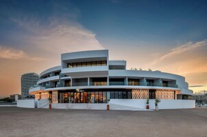 Un hotel moderno con fachada curva, varios balcones y una entrada destacada con fachada de vidrio.