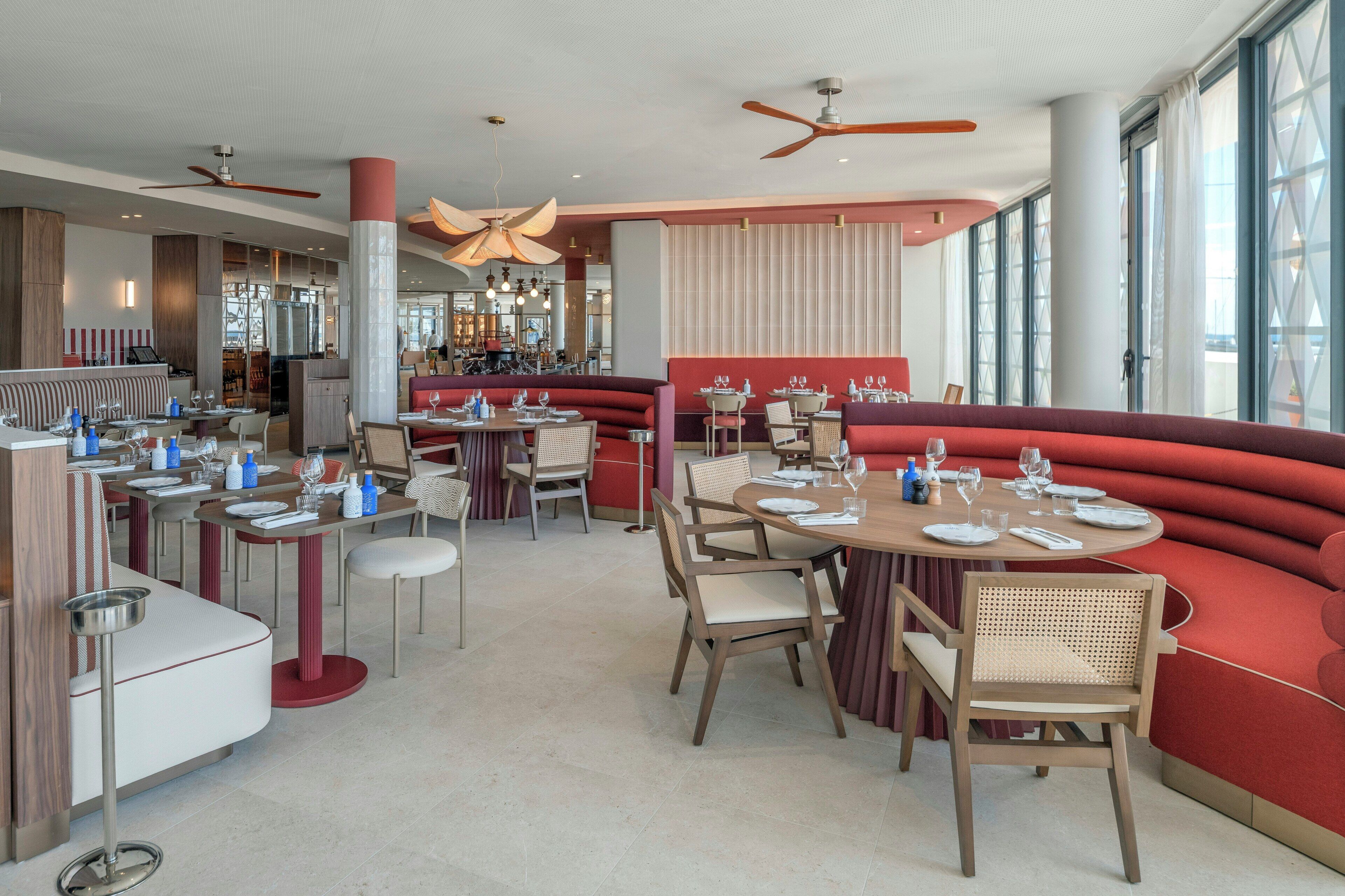 A modern restaurant interior with high ceilings, ceiling fans, and large windows.