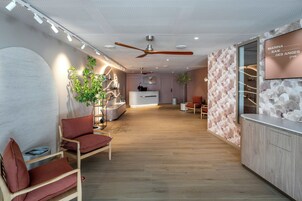 Zona de recepción moderna con un mostrador de madera, área de estar con cojines rojos y un televisor empotrado mostrando el nombre del spa.