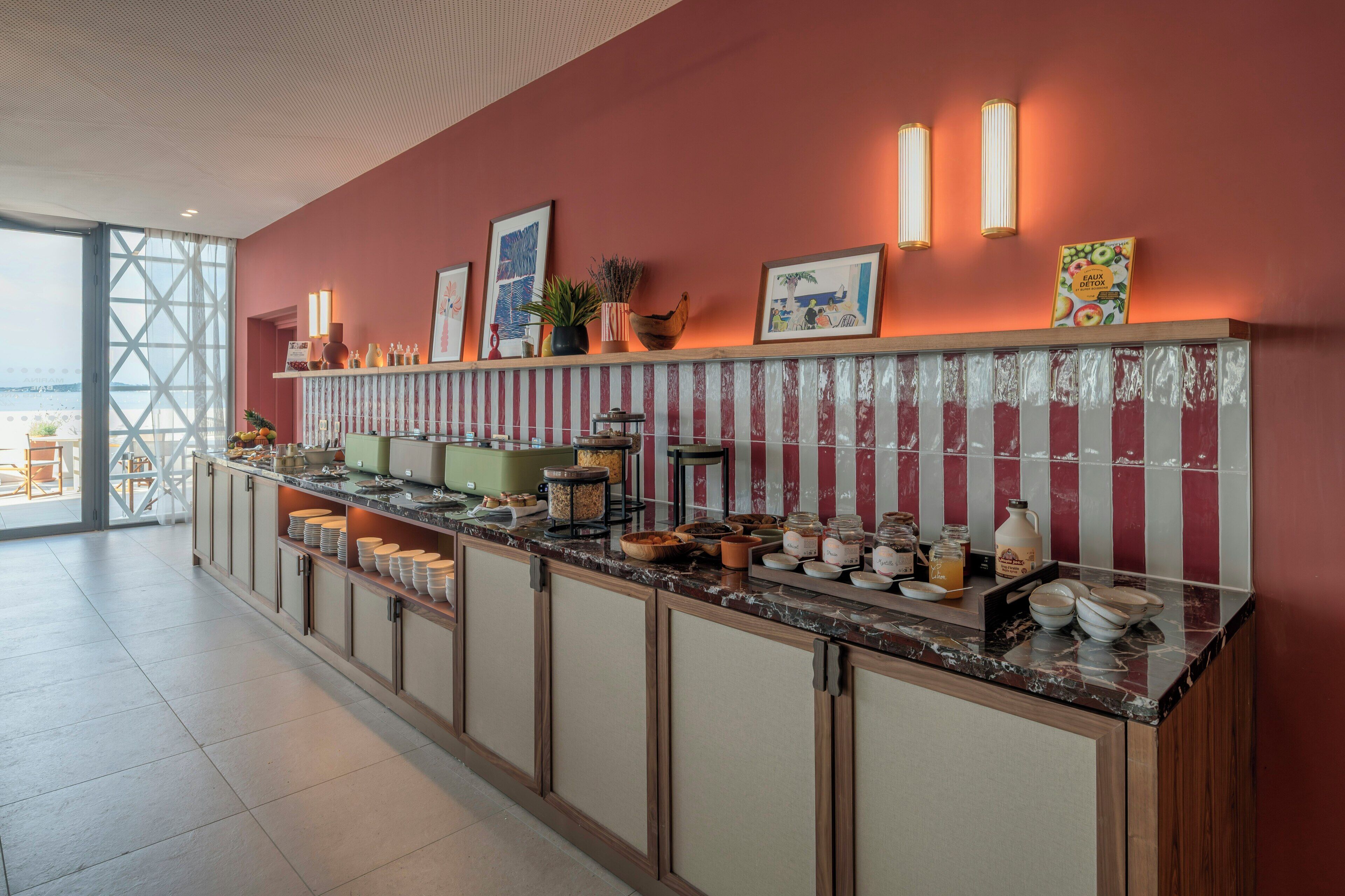 Zona de recepción de un hotel con una larga barra de mostrador, diversos alimentos y vista al mar a través de un amplio ventanal.