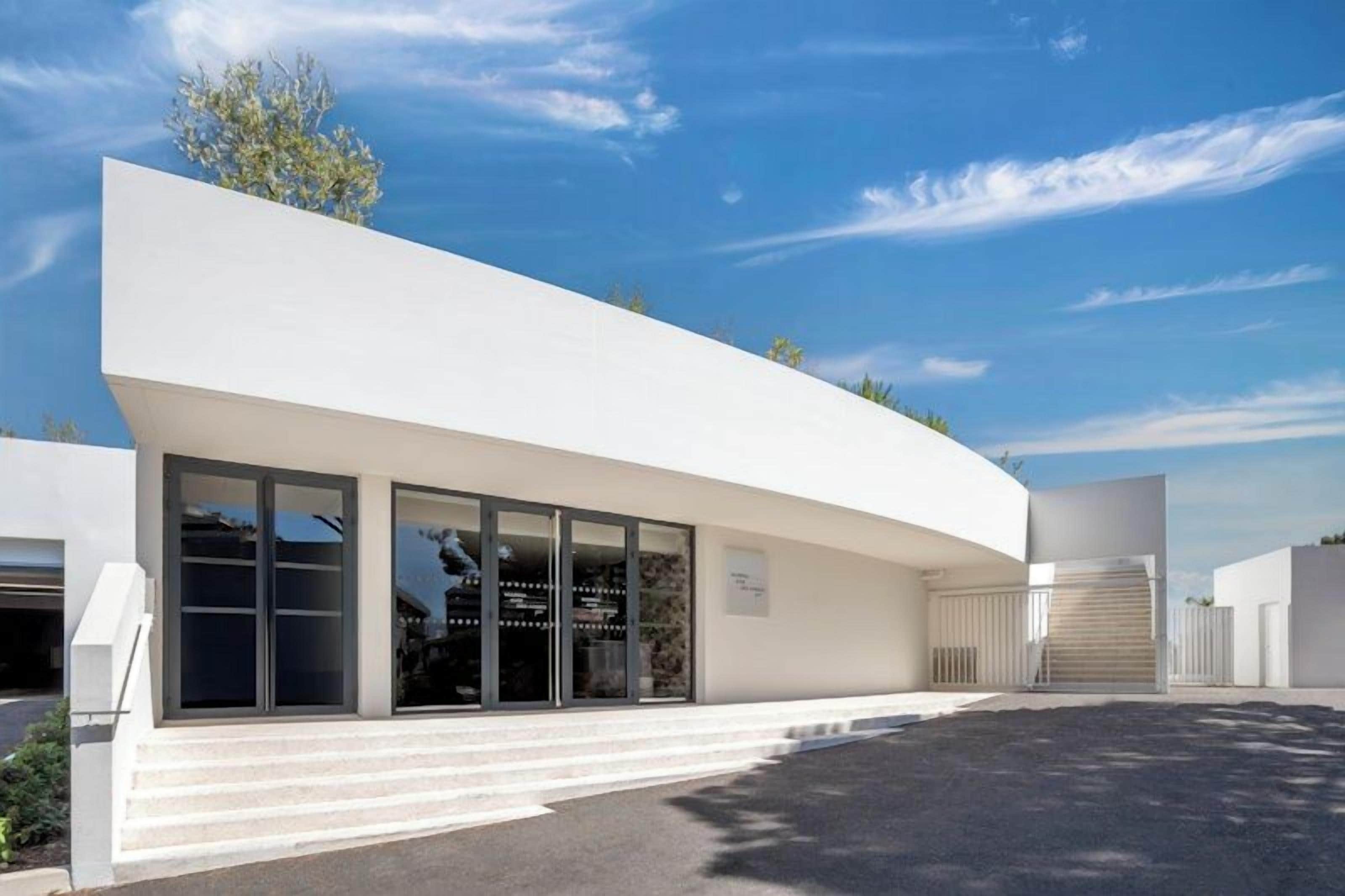 Un edificio moderno con fachada curva, ventanas amplias y una escalera que conduce a la entrada.