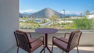 Un balcon avec deux chaises et une table, donnant sur un bâtiment moderne et un espace paysager aménagé.