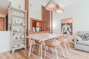 A dining area with a wooden table and wicker chairs, a bookshelf with decorative items, and a modern pendant light. - HAVN - Spacious One Bedroom in Downtown Dubai (Dubai)