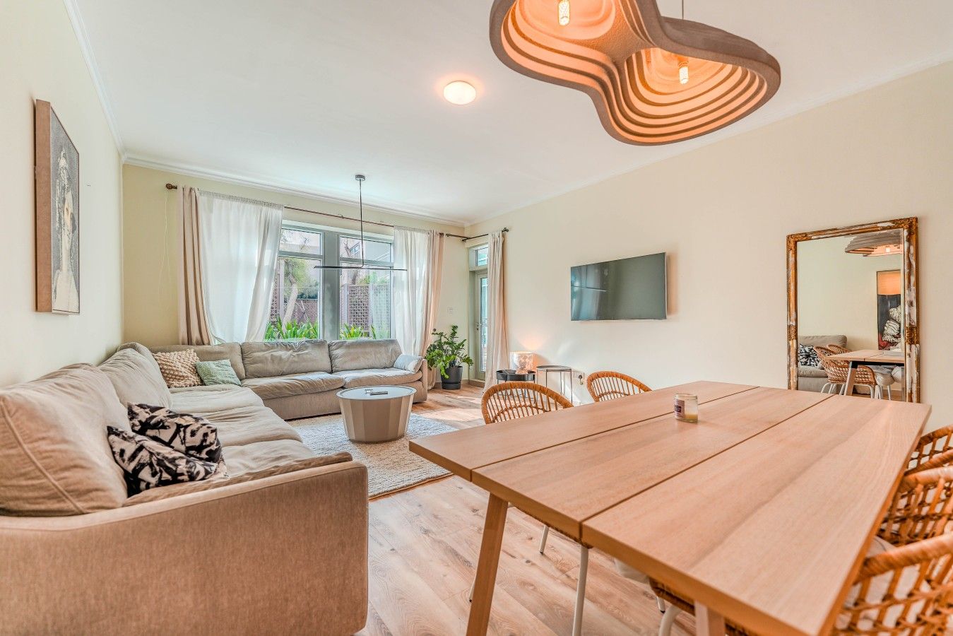 Een moderne woonkamer met een bank, een eettafel en een aan de muur bevestigde televisie.