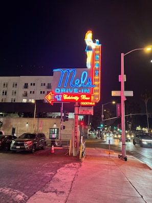 Neonverlicht bord voor 'Mels Drive-In Celebrity Bar' met autobediening.